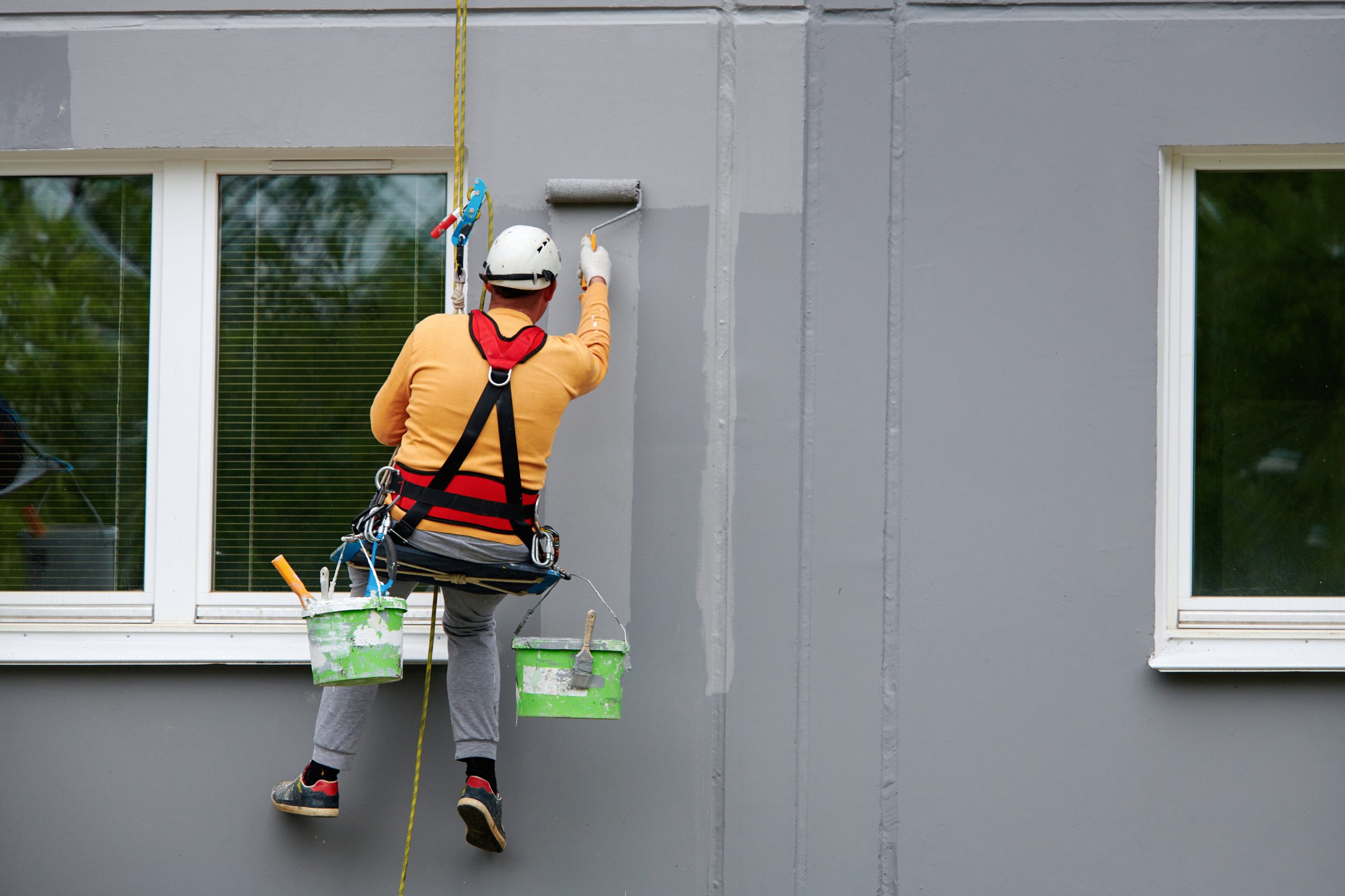 Worker,Hanging,On,Rope,And,Paints,Building,Wall,With,Roller.